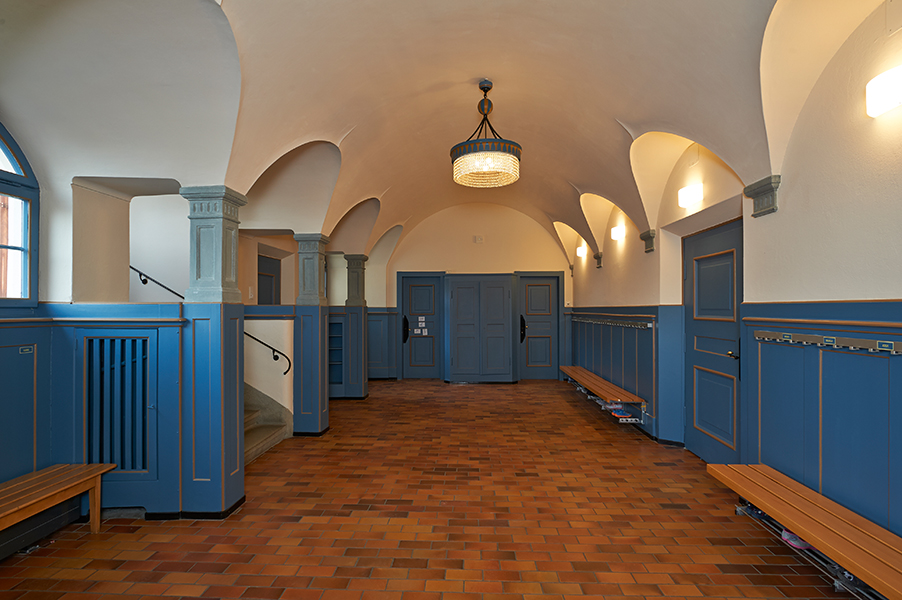 Pausenhalle im Erdgeschoss mit restauriertem Brusttäfer und historischem Leuchter